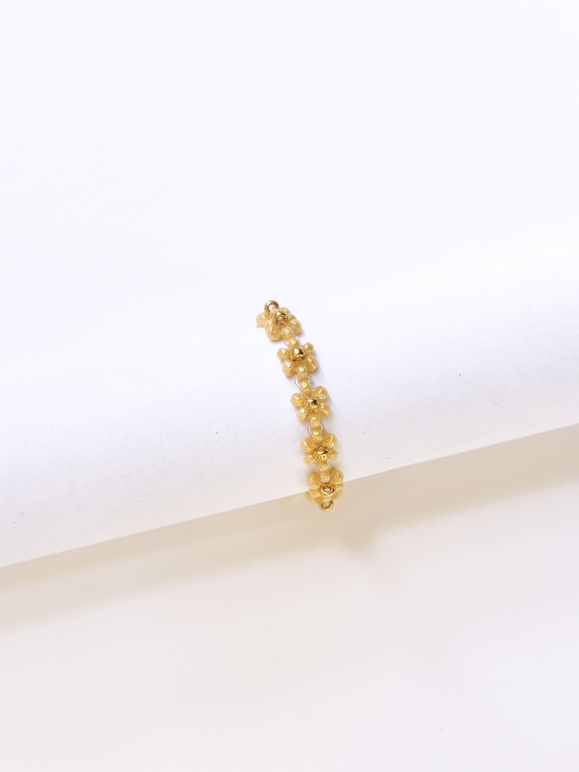 A delicate daisy chain ring made of premium gold and neutral-toned Japanese seed beads, displayed on a jewelry stand.
