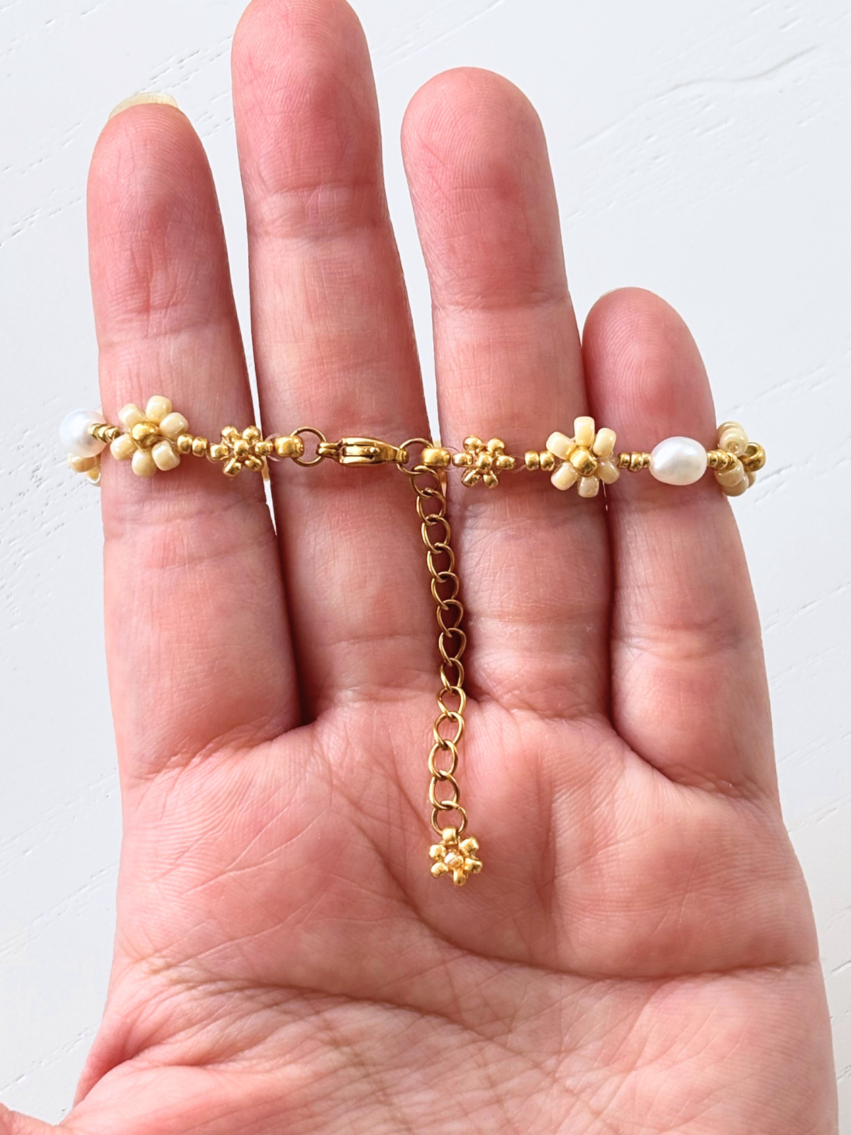 Close up of the dangling gold flower charm and adjustable extender chain on the August Pearl Bracelet.