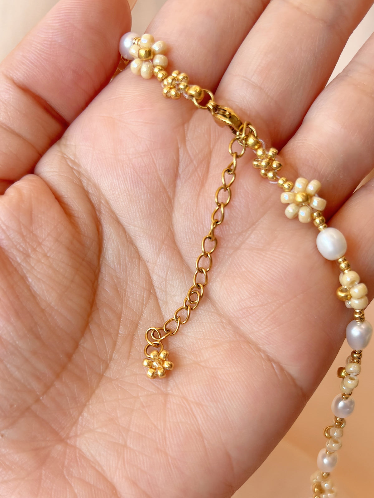 Close up of the dainty dangling gold daisy charm and adjustable extender chain on August Pearl necklace.