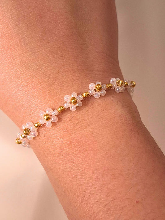 A close-up of a person's wrist wearing the delicate cream Daisy Bracelet (Dewdrop) with small flower motifs and luminous gold accents.
