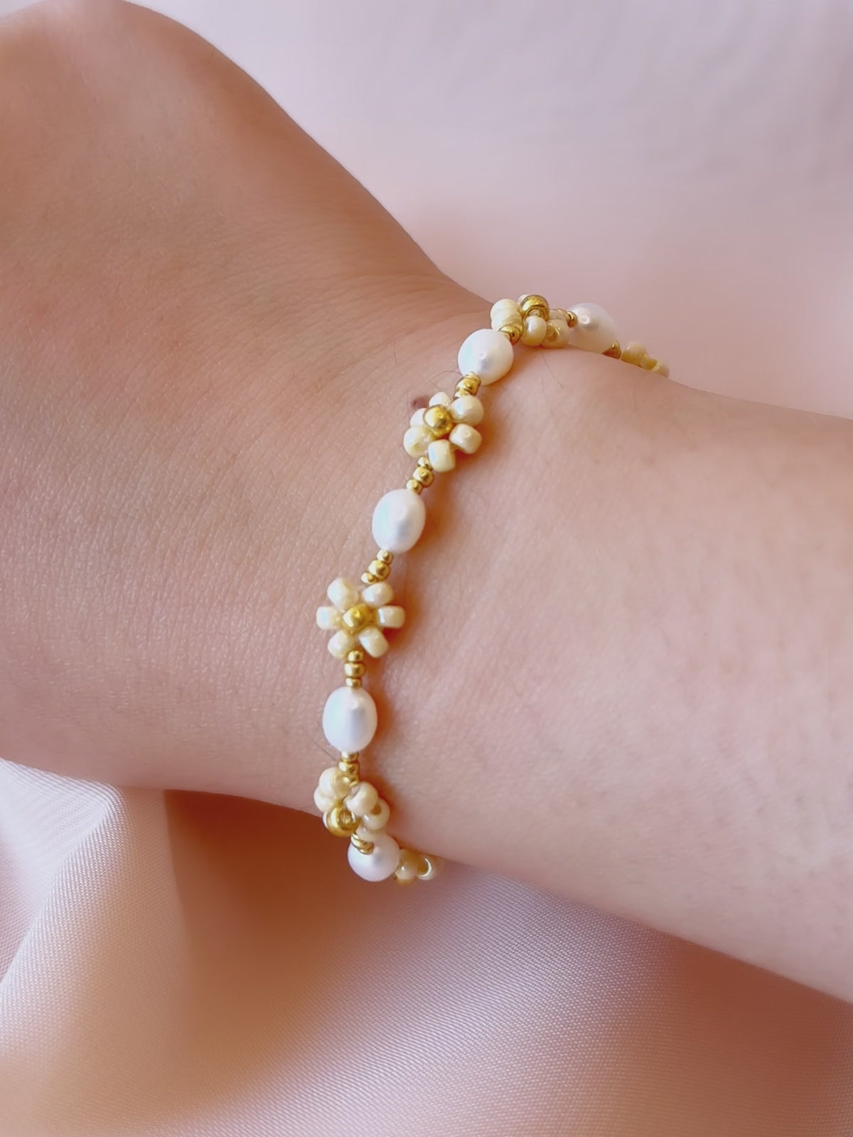 A video showcasing the August Pearl Bracelet worn on a wrist, highlighting the natural luster of freshwater pearls and sparkle of gold seed bead daisies.